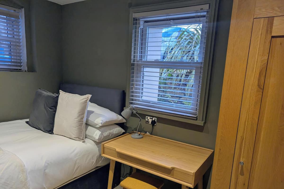 Un dormitorio con cama, escritorio, silla, ventana con persianas y armario.