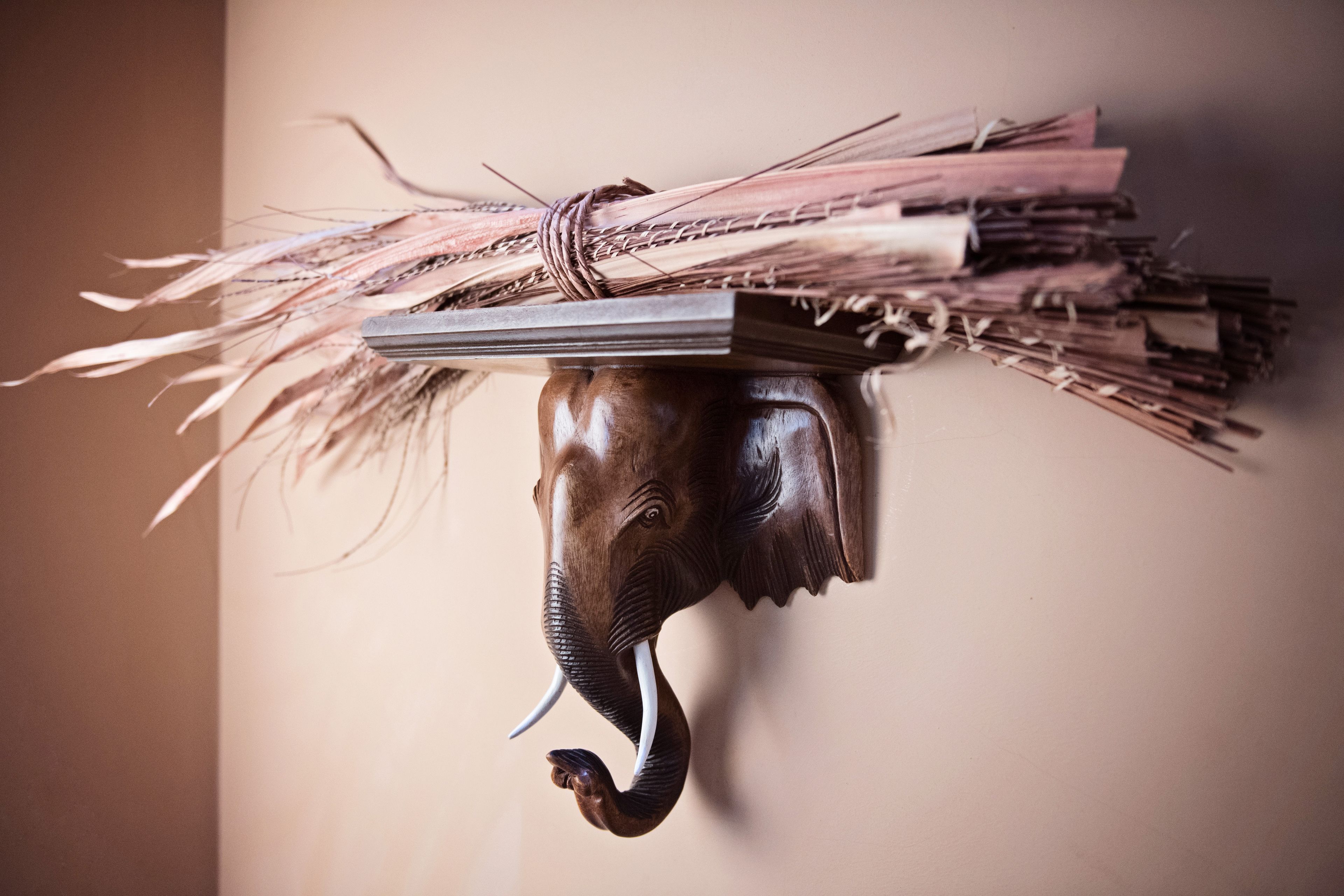 A wooden elephant head sculpture with a bundle of sticks hanging from its trunk.