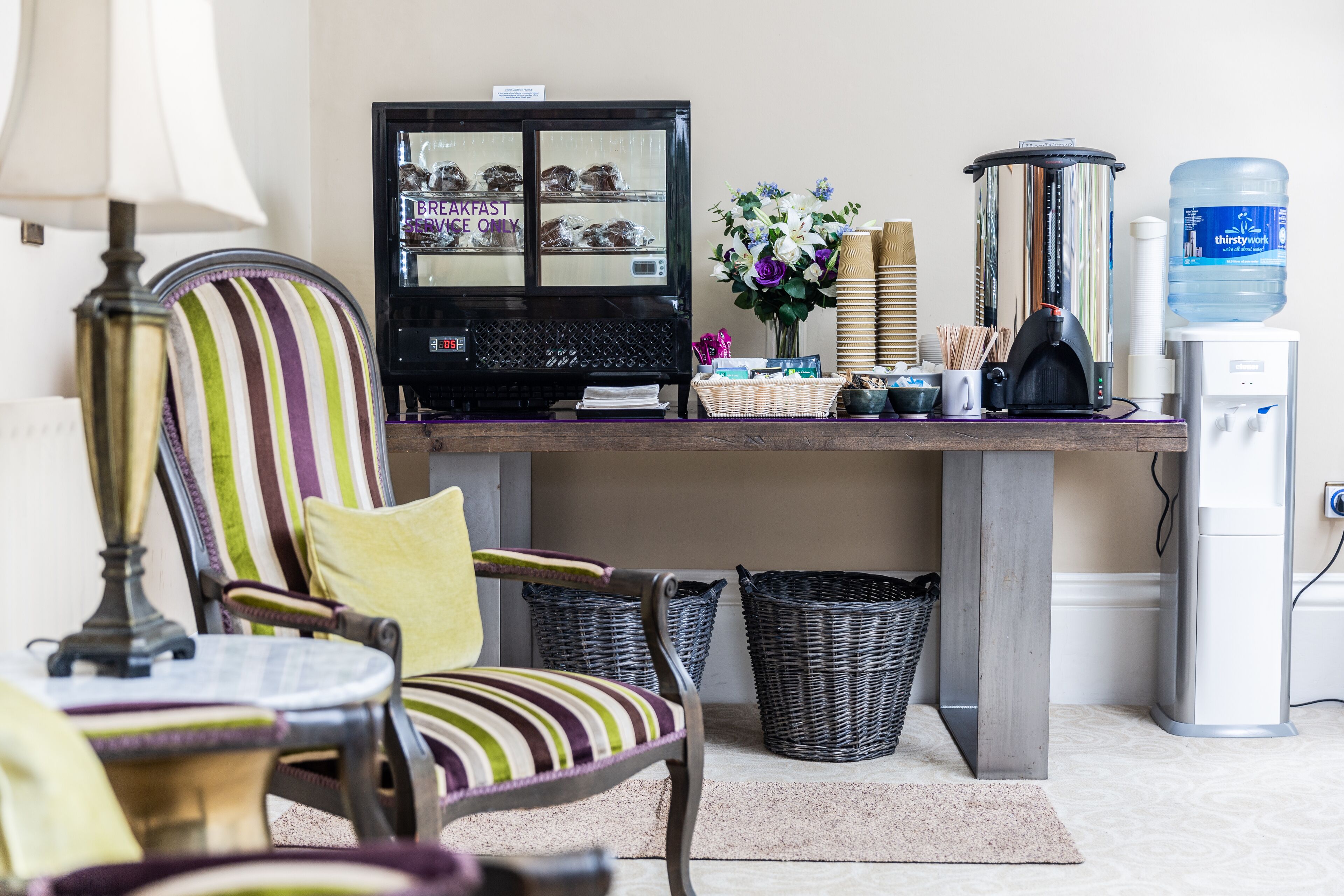 A breakfast bar with a refrigerator, wicker baskets, a water dispenser, and striped chairs.