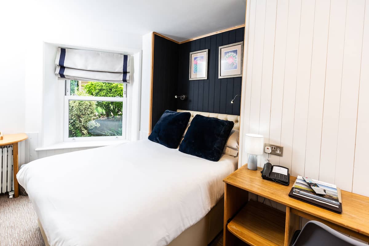 Un dormitorio ordenado con cama, mesita de noche, lámpara y un pequeño escritorio con silla.