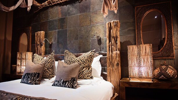 A bedroom with a large bed, multiple pillows, a wooden nightstand, a mirror, and a textured wall. - Beaumont House (Cheltenham)