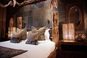 A bedroom with a large bed, multiple pillows, a wooden nightstand, a mirror, and a textured wall. - Beaumont House (Cheltenham)