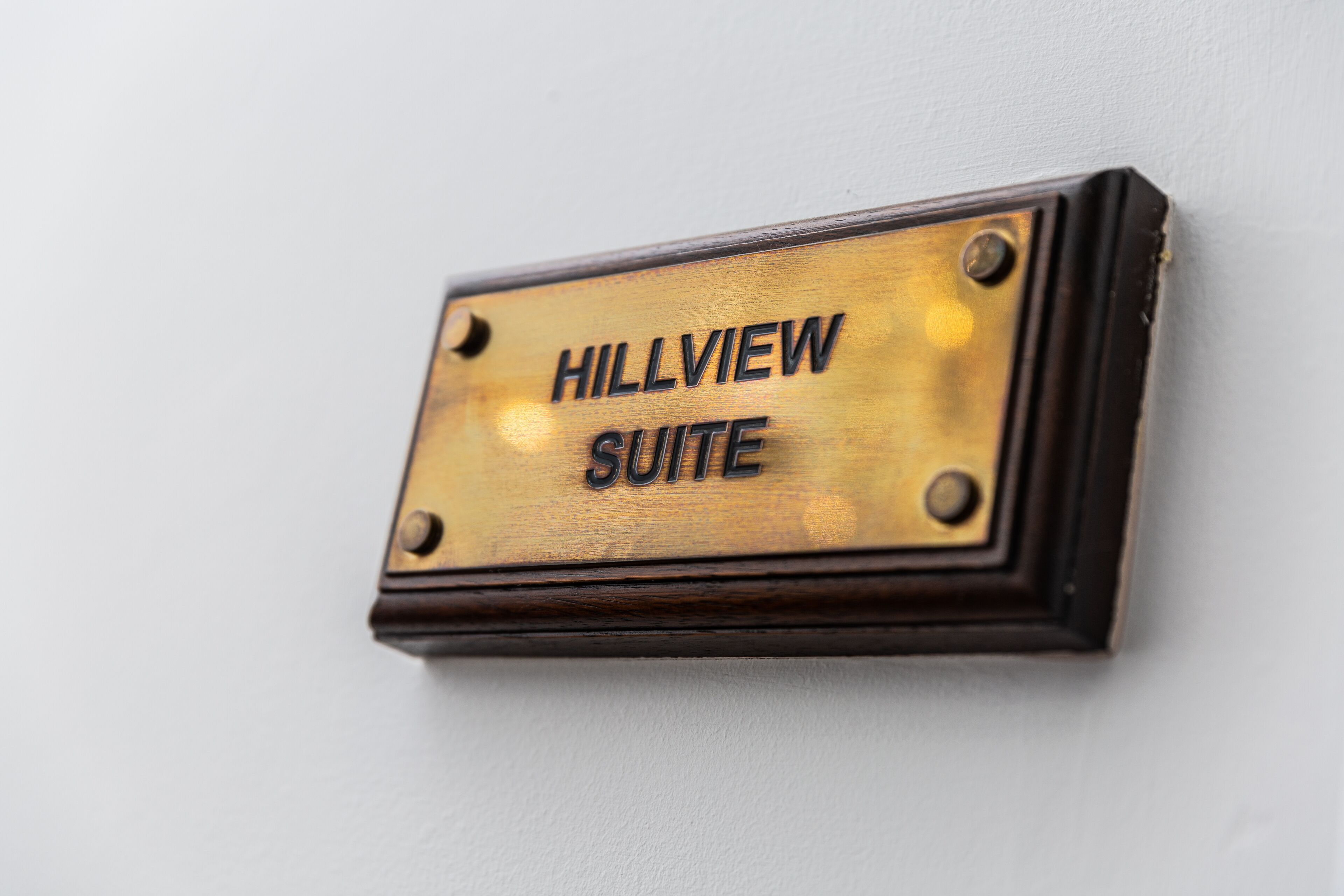 Eine bronzene Schild mit der Aufschrift „HILLVIEW SUITE“ ist an einer Wand angebracht.