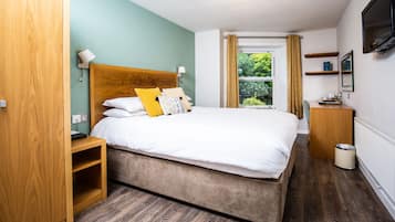 A bedroom with a bed, bedside table, lamp, TV, and a window with curtains.