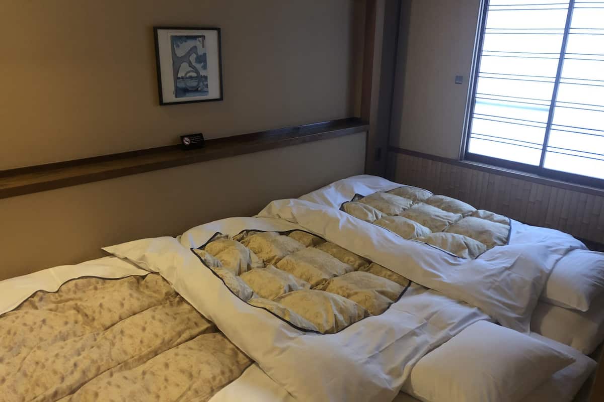 A hotel room with two beds, a framed picture on the wall, and a window with blinds.