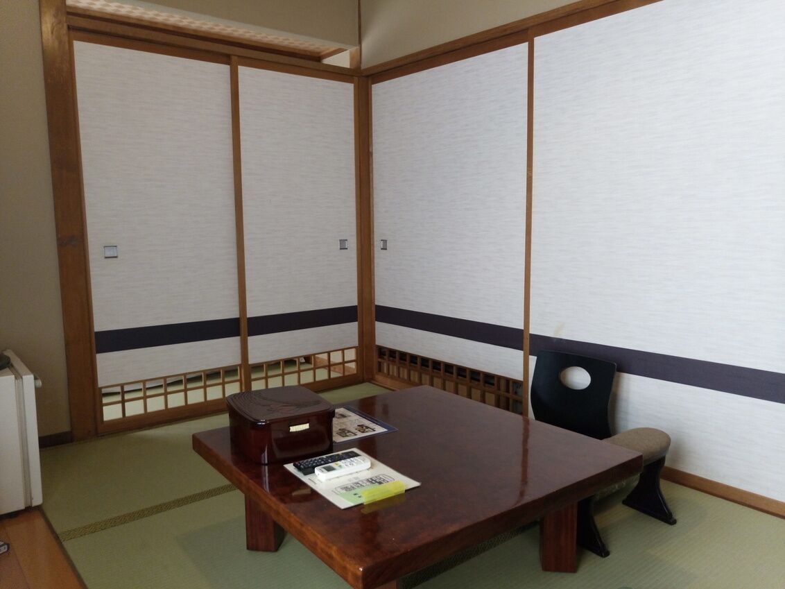 Una habitación japonesa tradicional con suelo de tatami, una mesa de madera baja, una silla y puertas correderas shoji.