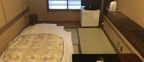 Een hotelkamer met een bed, een televisie, een kleine kitchenette en een raam met zonwering.