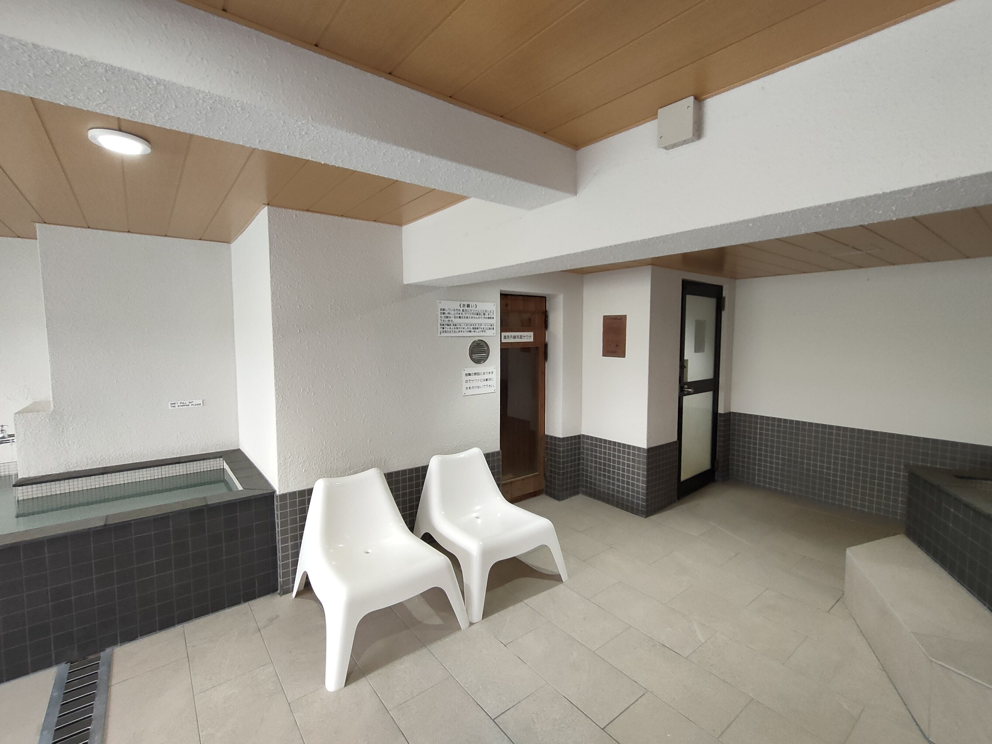 A waiting area with a reception desk, a reception sign, a door, and two white plastic chairs.