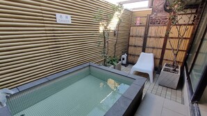 Une petite piscine extérieure entourée d’une clôture en bambou, avec une chaise en plastique blanche et un panneau indiquant « DANGER ».