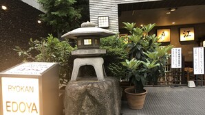 Une lanterne en pierre et une enseigne indiquant l’emplacement du Ryokan Edoya, le tout entouré de plantes en pot et situé près de l’entrée du bâtiment.