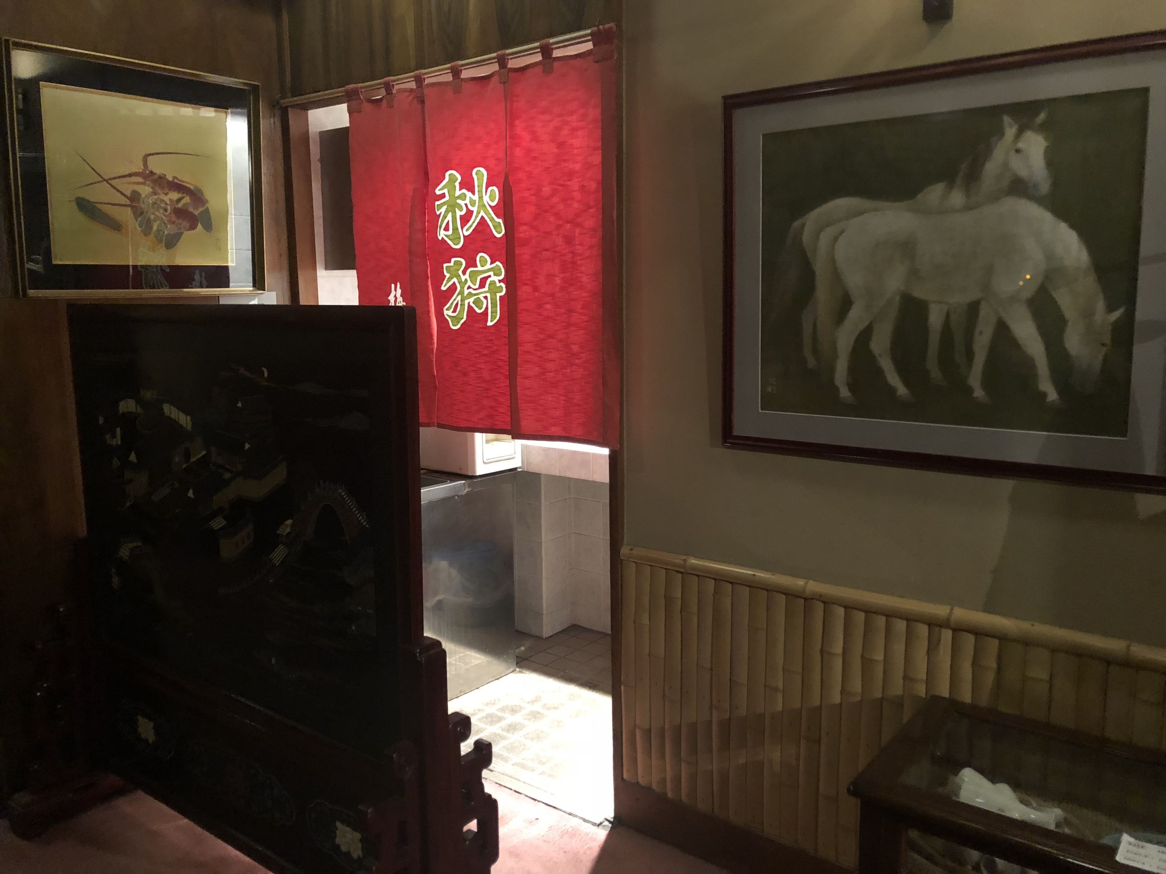 Una habitación con un cuadro enmarcado de un caballo, una cortina roja con caracteres chinos y un radiador.