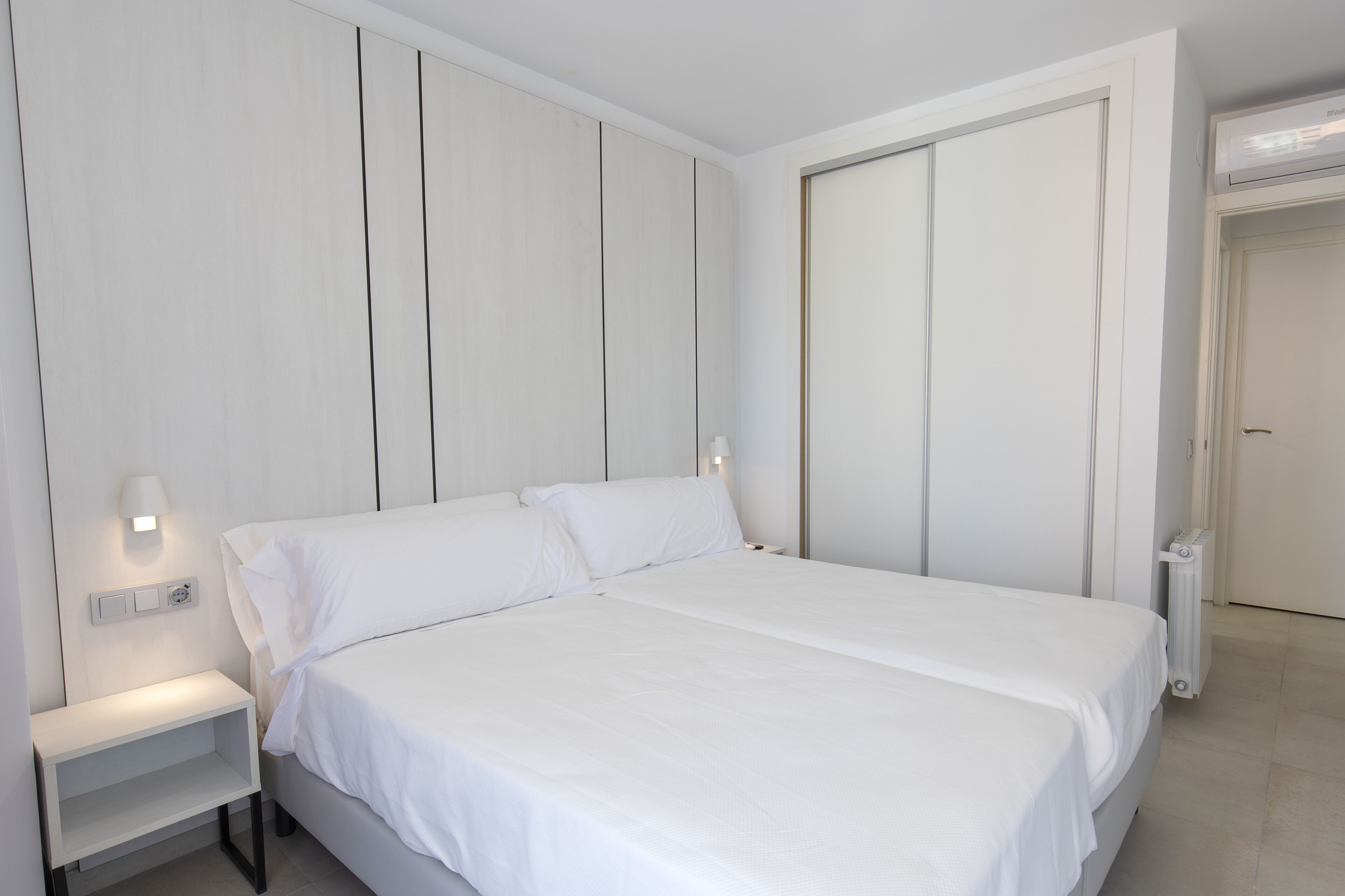 Une chambre à coucher avec un lit, une table de chevet, une lampe fixée au mur et une porte.