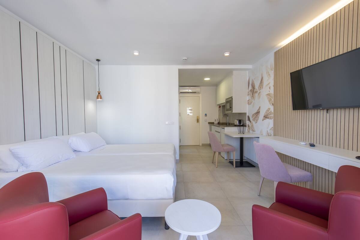 Una habitación de hotel moderna con una cama, un escritorio, un televisor y sillas rojas y rosas.