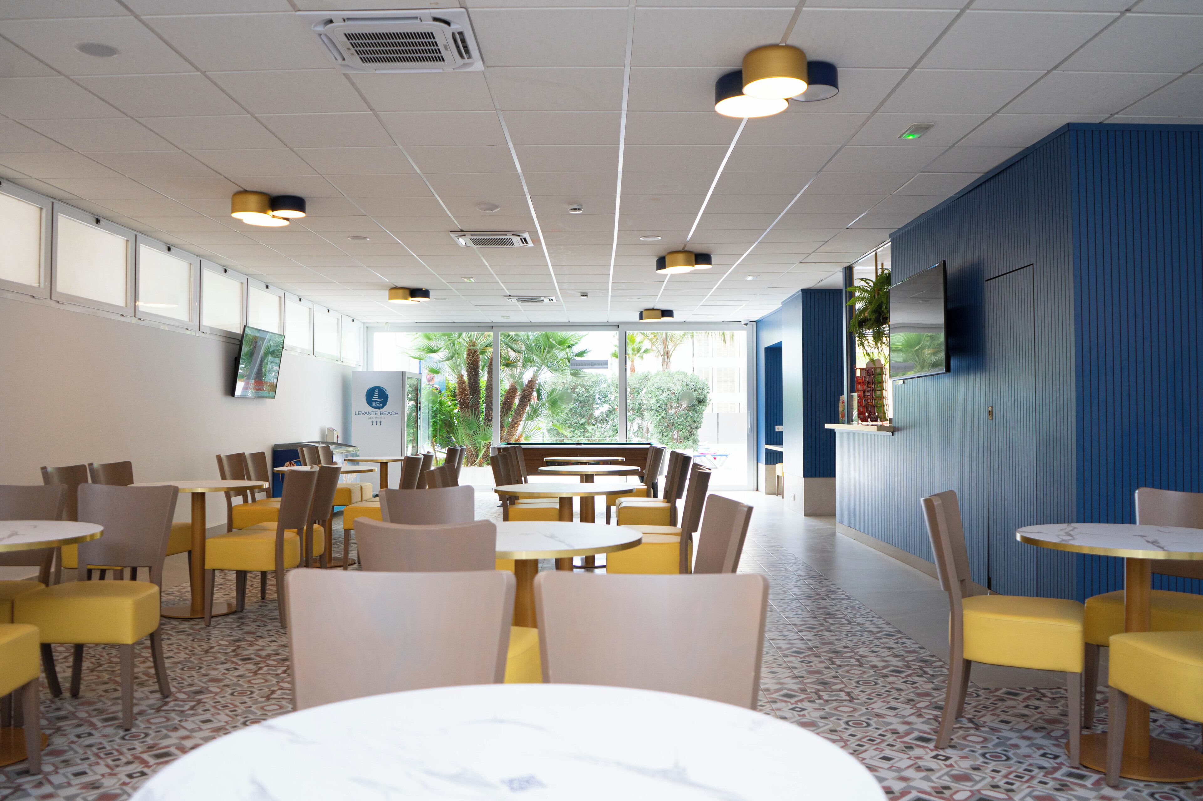 A spacious indoor dining area with multiple tables and chairs, large windows allowing natural light, and a blue accent wall.