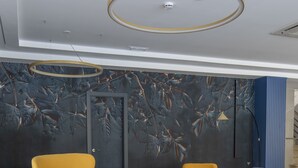 Un área de descanso moderna con sillas de color amarillo y azul intenso, una mesa redonda e iluminación circular en el techo.