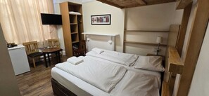 Una habitación de hotel con cama, escritorio, silla, televisor y estante.