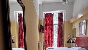 A hotel room with two beds, a large mirror, a wooden floor, a window with red curtains, and a hanging light fixture. - Dolphin Inn (London)