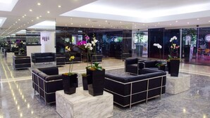 Un hall d’entrée moderne avec des canapés noirs, un sol en marbre et de grands pots d’orchidées.