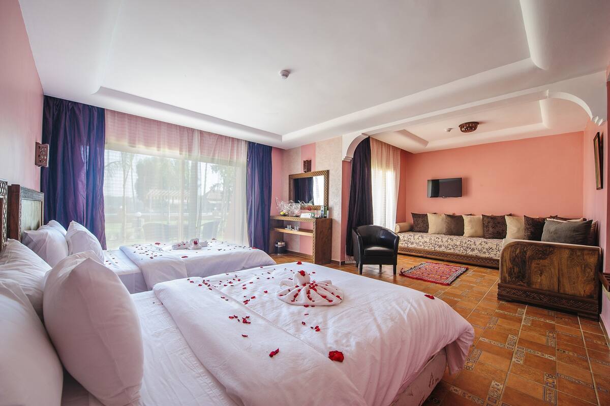 Quarto de hotel com duas camas, um sofá, uma escrivaninha e uma televisão.