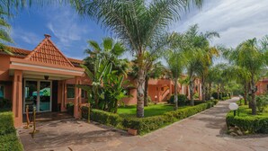 Un resort con un sendero pavimentado, palmeras y un edificio de techo a teja.