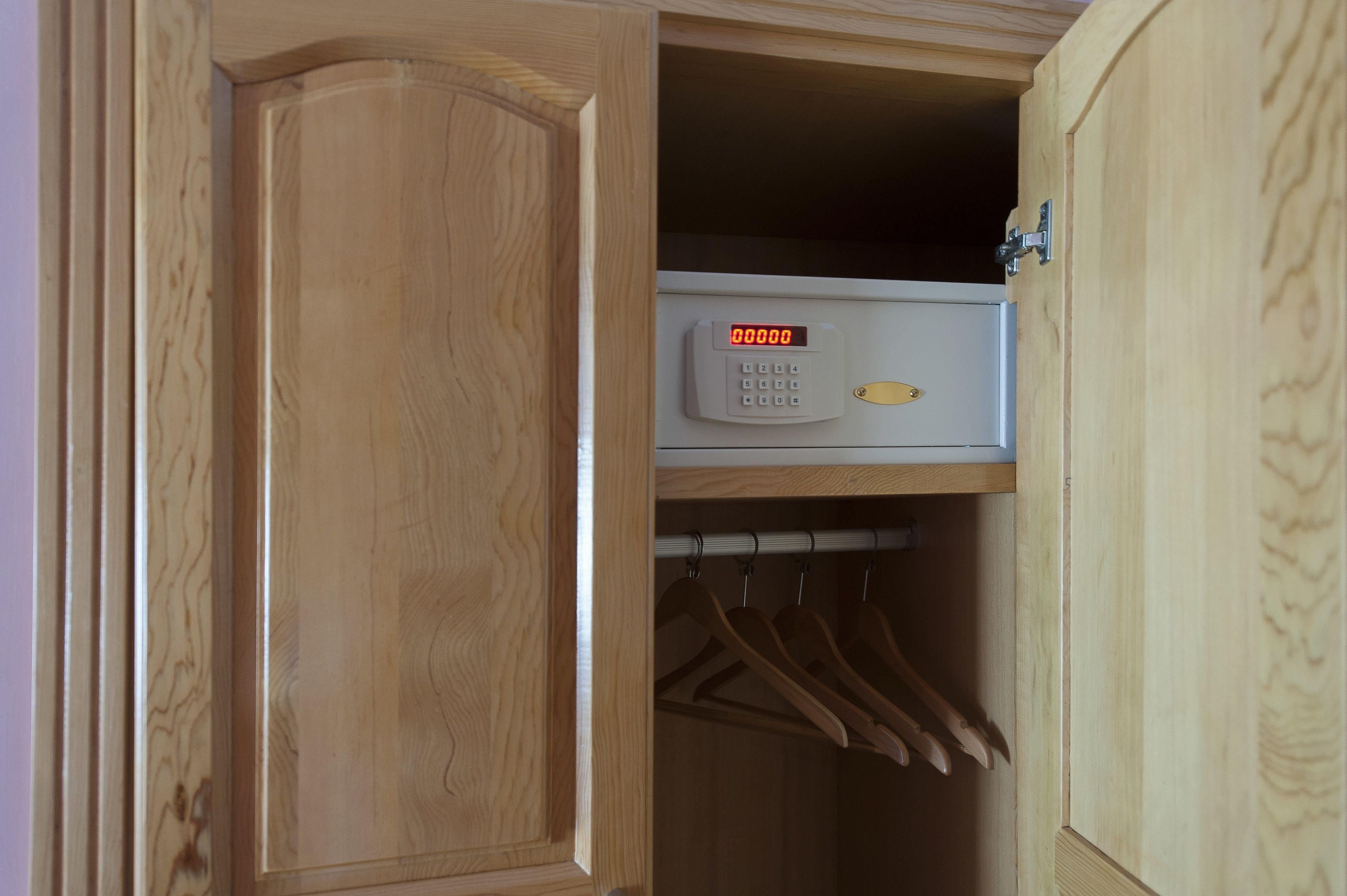 Un armario de madera con cerradura digital y perchas en su interior.