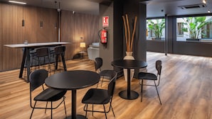 Un interior moderno con un panel de madera, una zona de bar y mesas redondas con sillas.