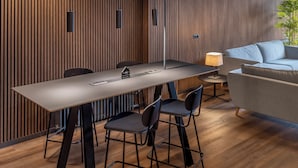 Una sala de reuniones moderna con una larga mesa, cuatro sillas, un sofá y una lámpara.