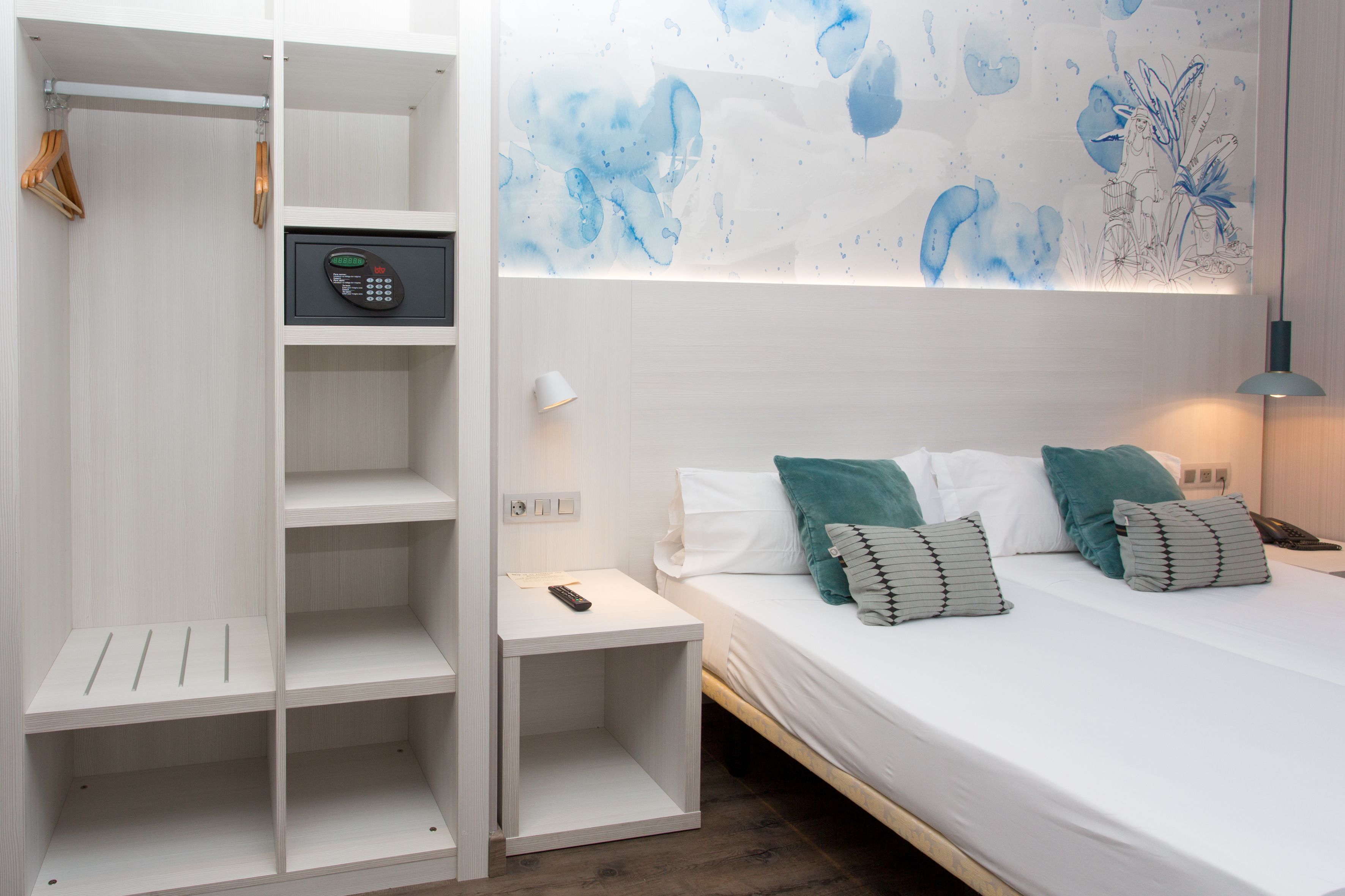 A bedroom with a bed, a nightstand, a wardrobe, and a wall with a blue abstract design.