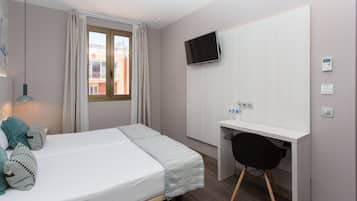 Hotelkamer met een bed, een bureau, een stoel, een televisie en een raam met gordijnen.
