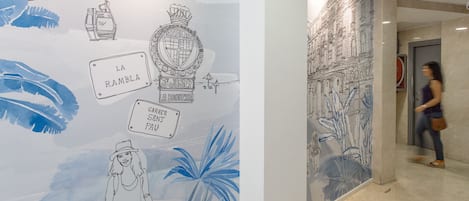 A hallway with a mural featuring architectural drawings and text labels like "LA RAMBLA" and "LA BOUQUERIA."