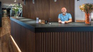Un mostrador de recepción con diseño moderno, que destaca por un panel de madera y una iluminación colgante.