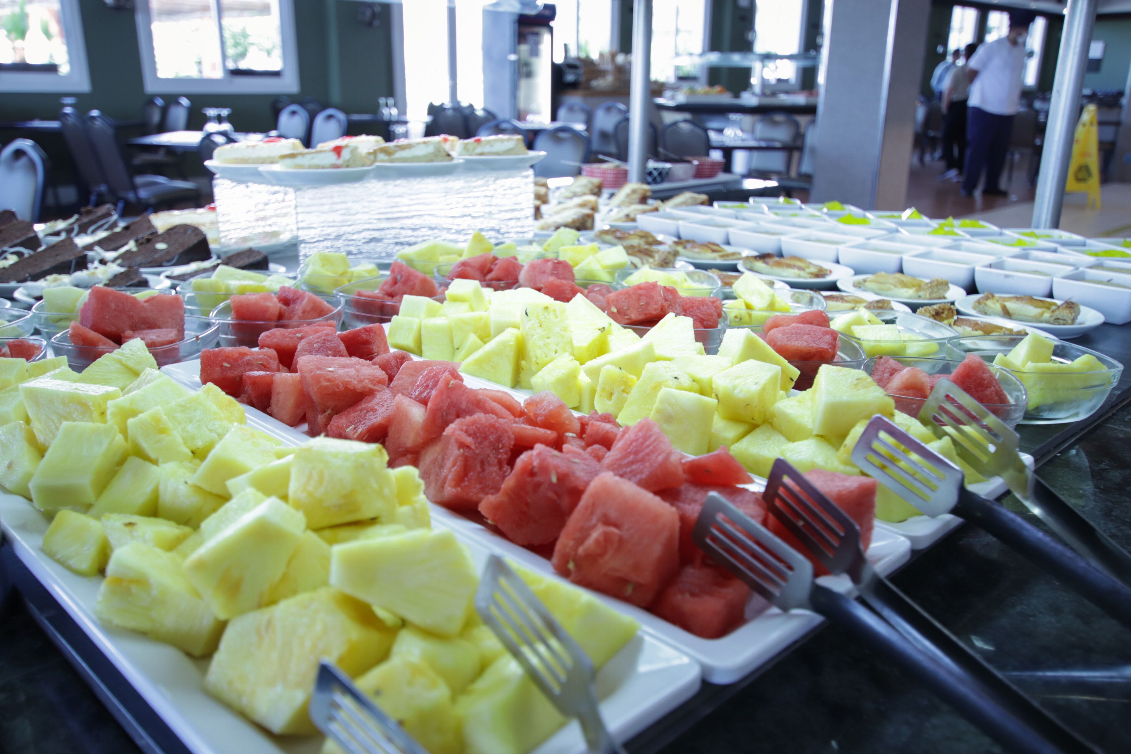 A buffet with various fruits and a dining area in the background.