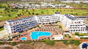 A hotel with multiple buildings, a swimming pool, and a golf course in the background. - Ohtels Cabogata (Almeria)
