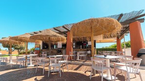 An outdoor patio with white tables and chairs, thatched umbrellas, and a bar area. - Ohtels Cabogata (Almeria)