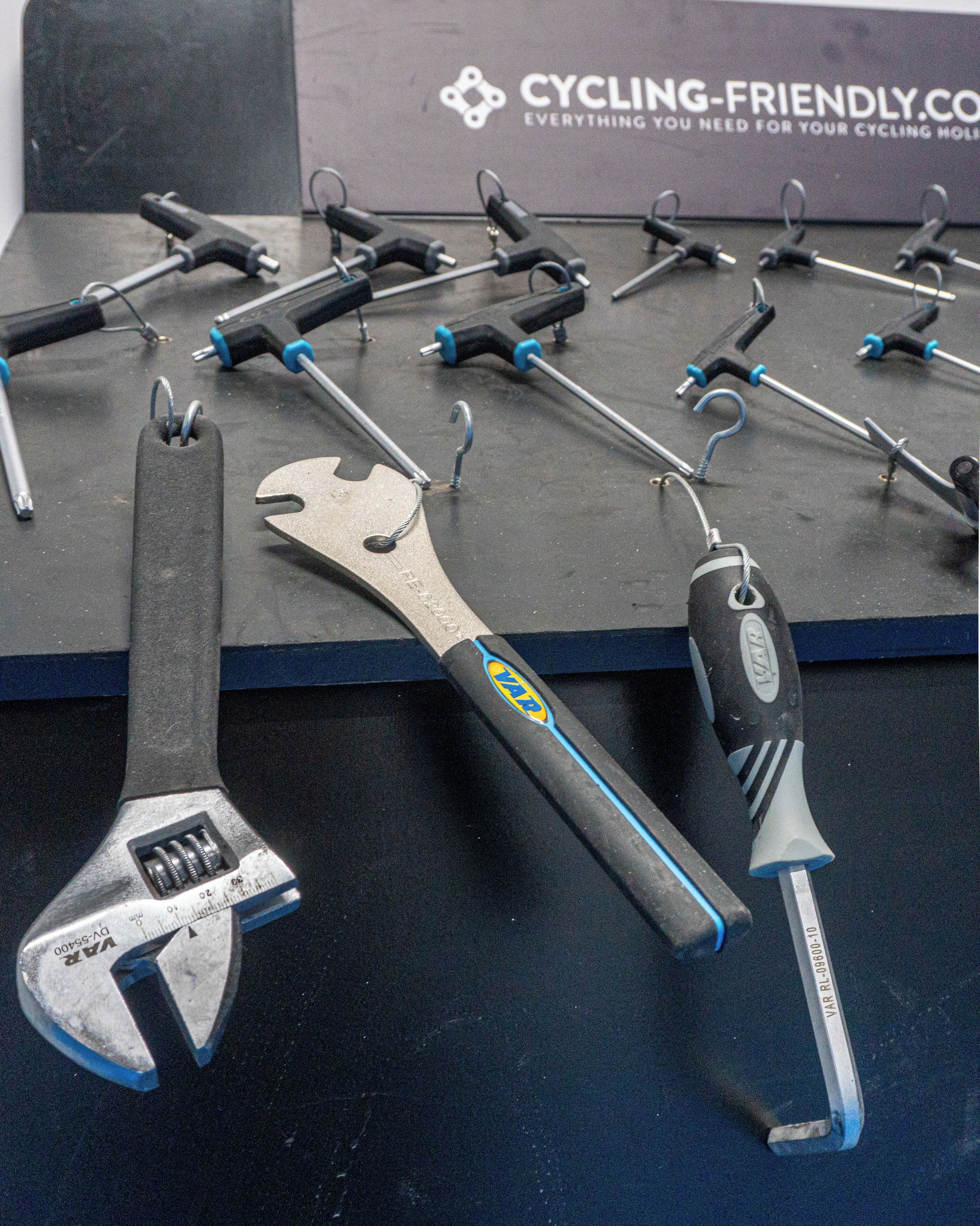 A display of tools including a wrench and a screwdriver with a blue handle, arranged on a black surface with a sign in the background reading "CYCLING-FRIENDLY.COM".