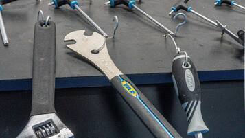 A display of tools including a wrench and a screwdriver with a blue handle, arranged on a black surface with a sign in the background reading "CYCLING-FRIENDLY.COM".