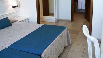 A bedroom with a bed, bedside table, and a chair. There is a bathroom visible through an open door.