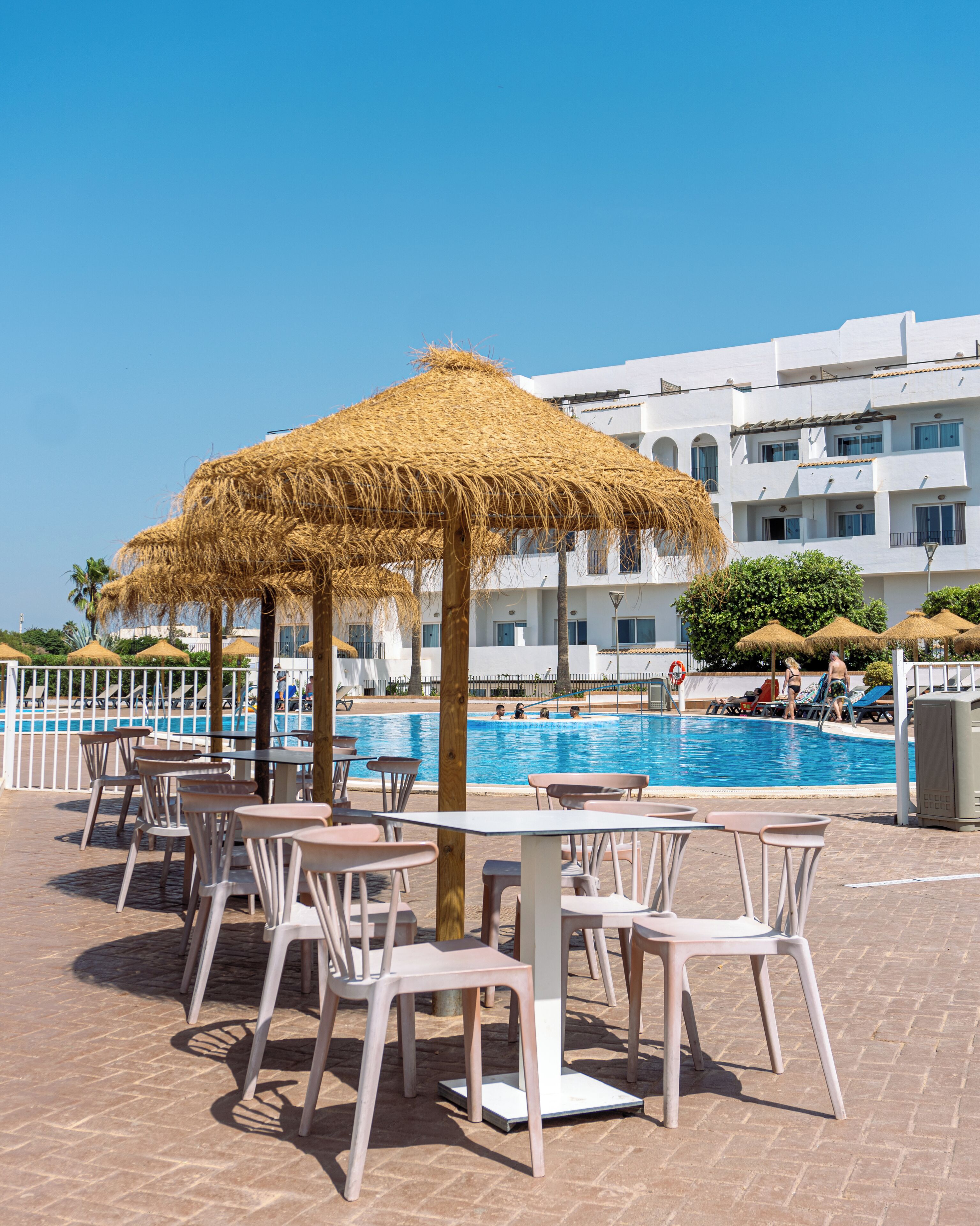 A poolside area with thatched umbrellas, lounge chairs, and a swimming pool.