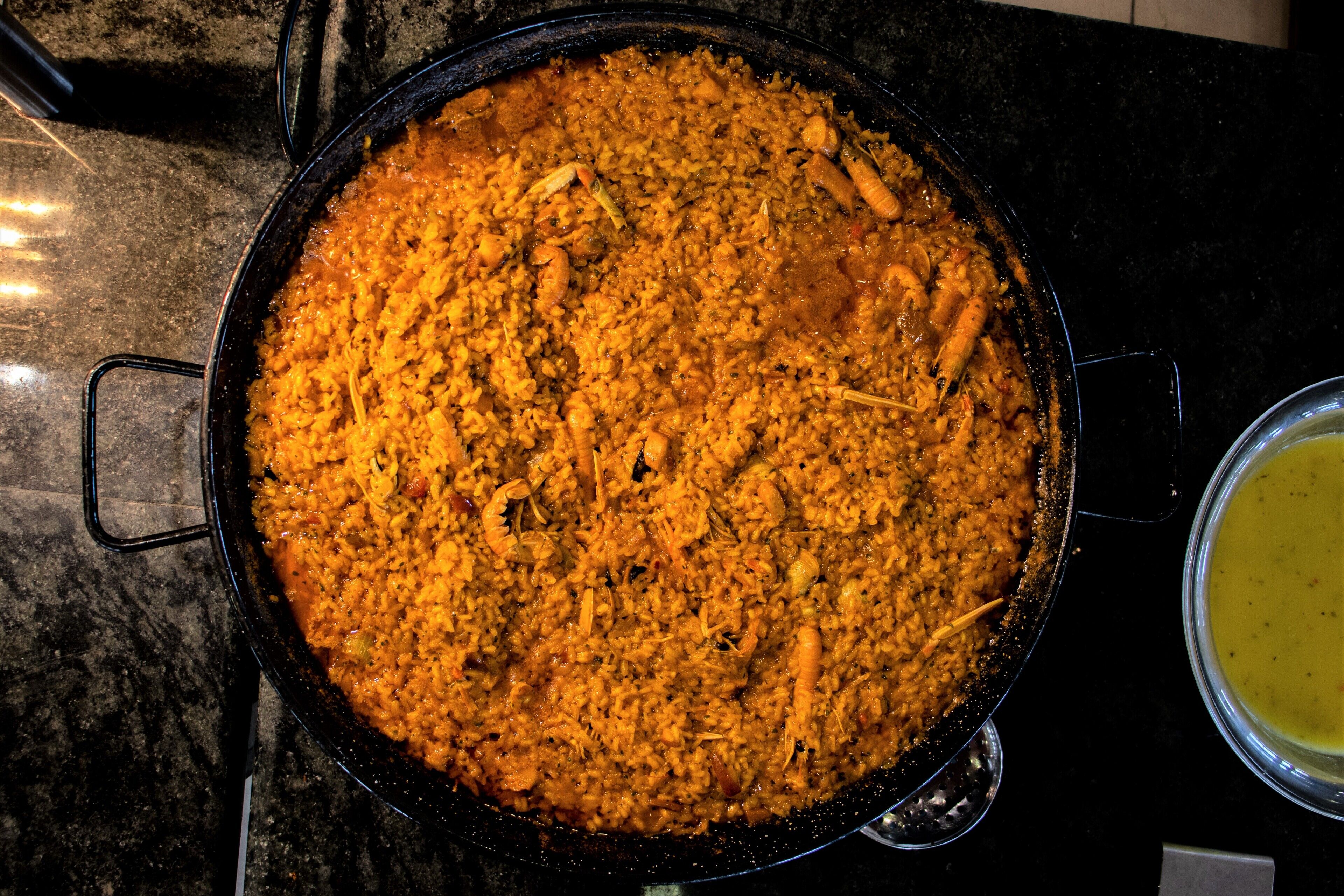 A large black pot filled with a dish, possibly rice, on a dark countertop.