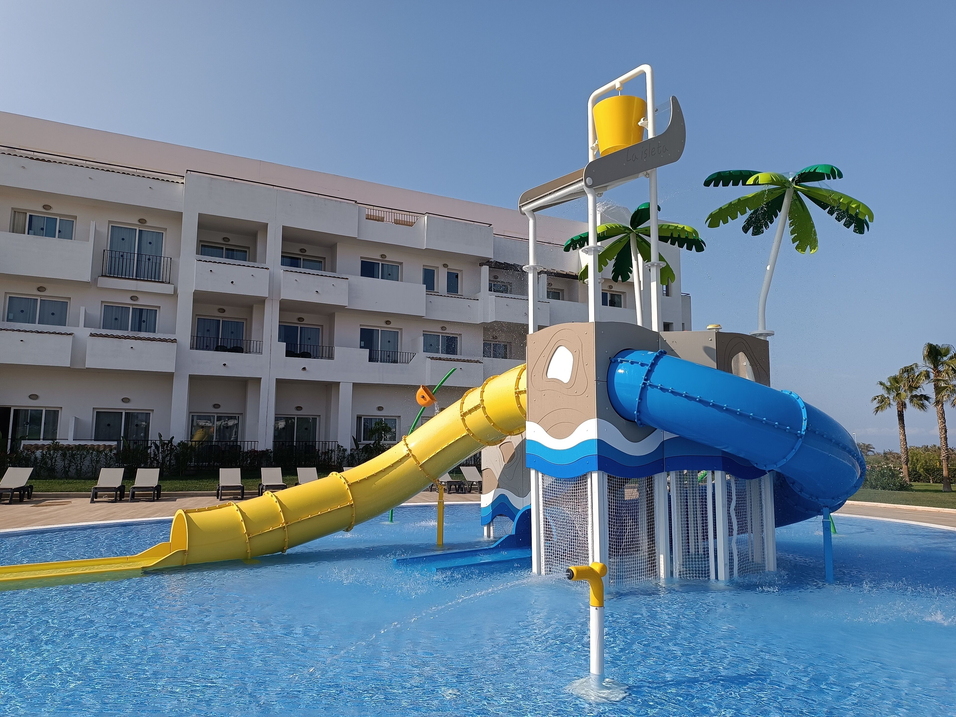 A water park with slides and a pool, surrounded by a multi-story building with balconies.