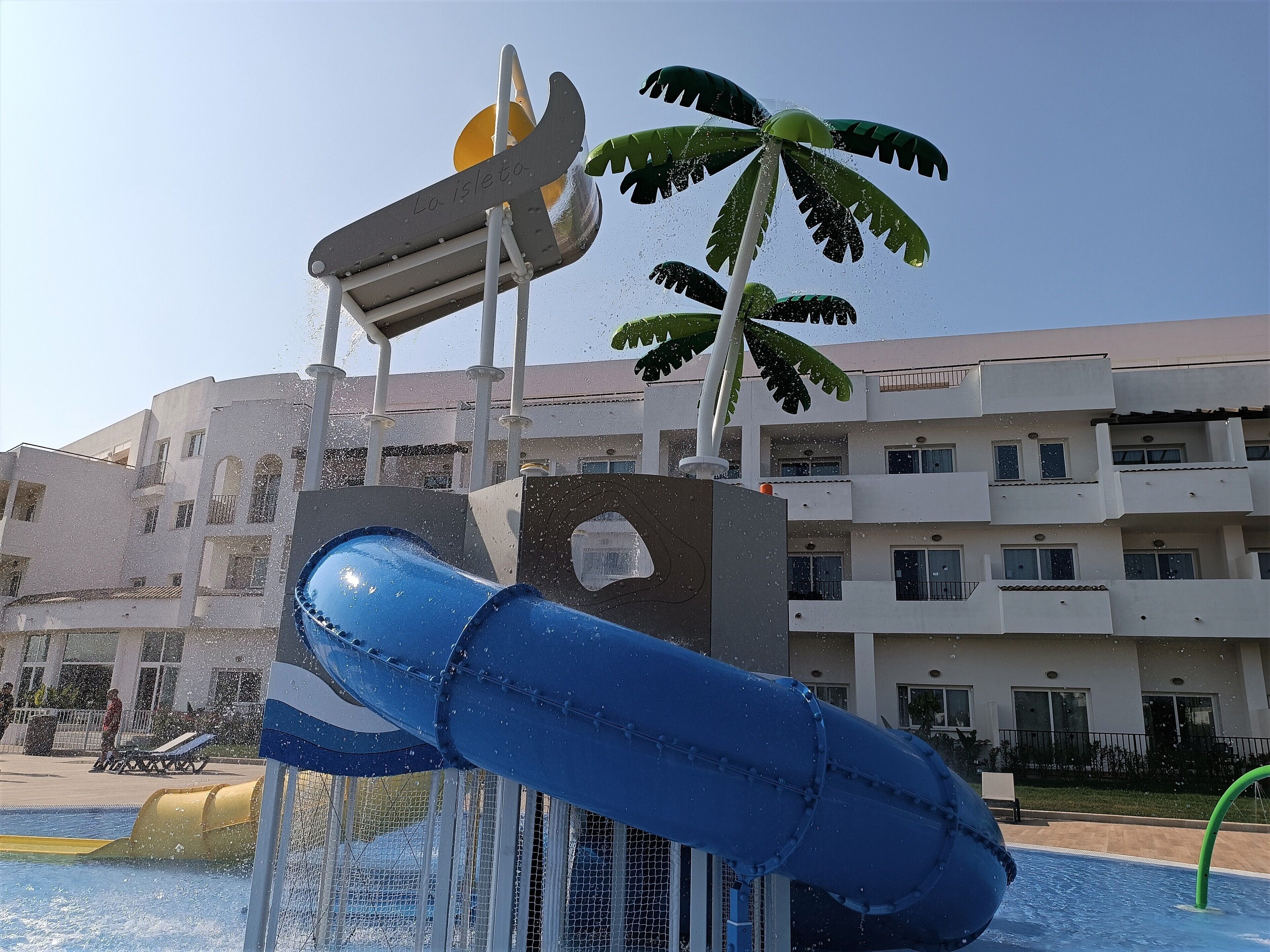 A water slide with a palm tree and a building in the background.