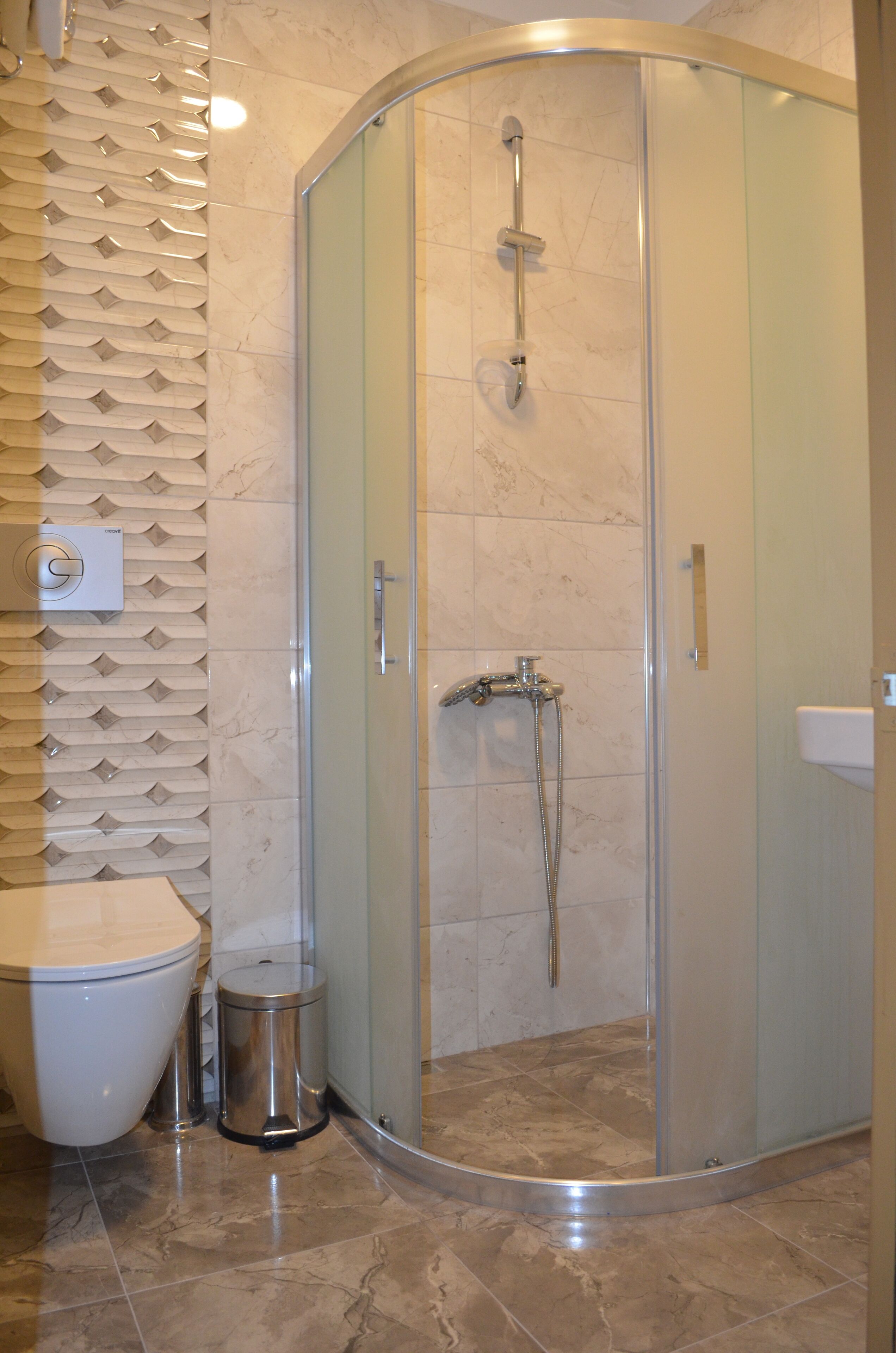 Un baño moderno con ducha de vidrio, inodoro y cubo de basura.