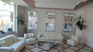 A living room with a white sofa set, a coffee table, and two potted plants. - Grand Milano Hotel (Ayvalik)