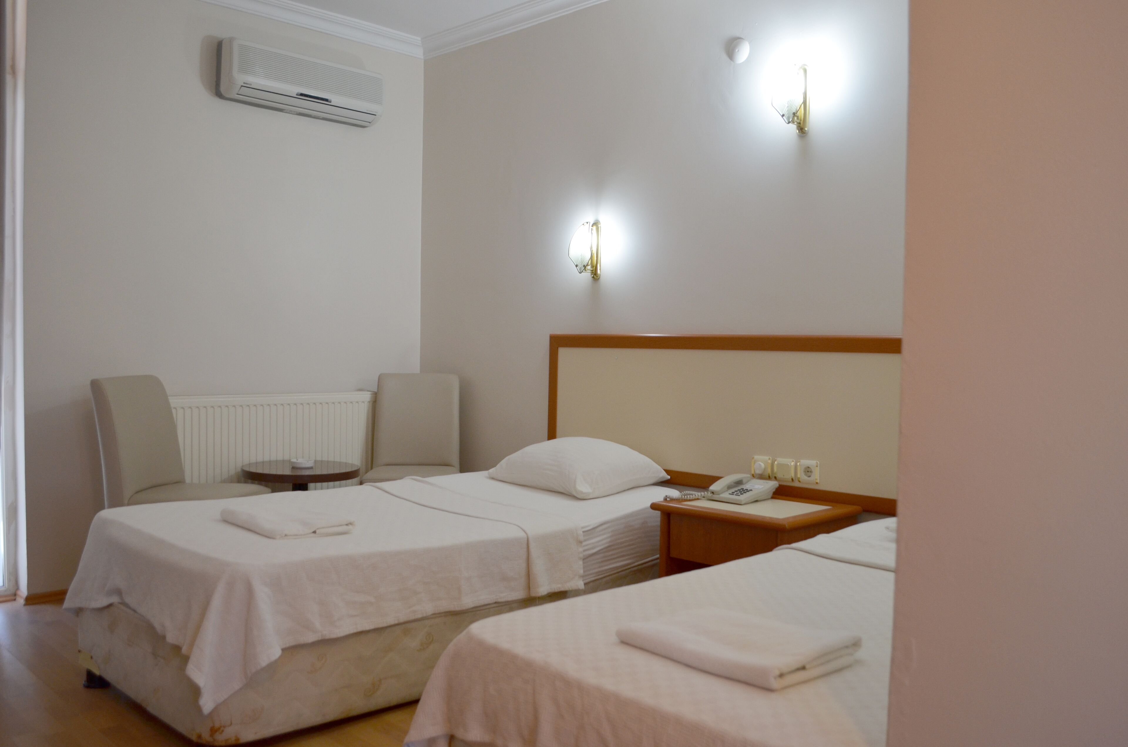 A hotel room with two beds, a bedside table with a phone, and a wall-mounted air conditioner.