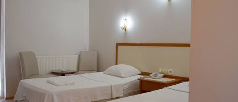 A hotel room with two beds, a bedside table with a phone, and a wall-mounted air conditioner.