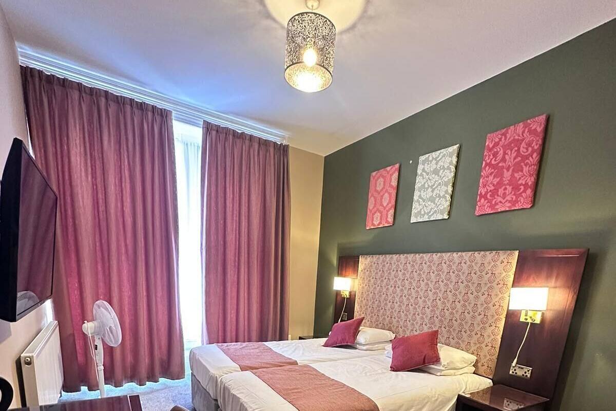 A hotel room with a large bed, a desk, a chair, and a ceiling light.