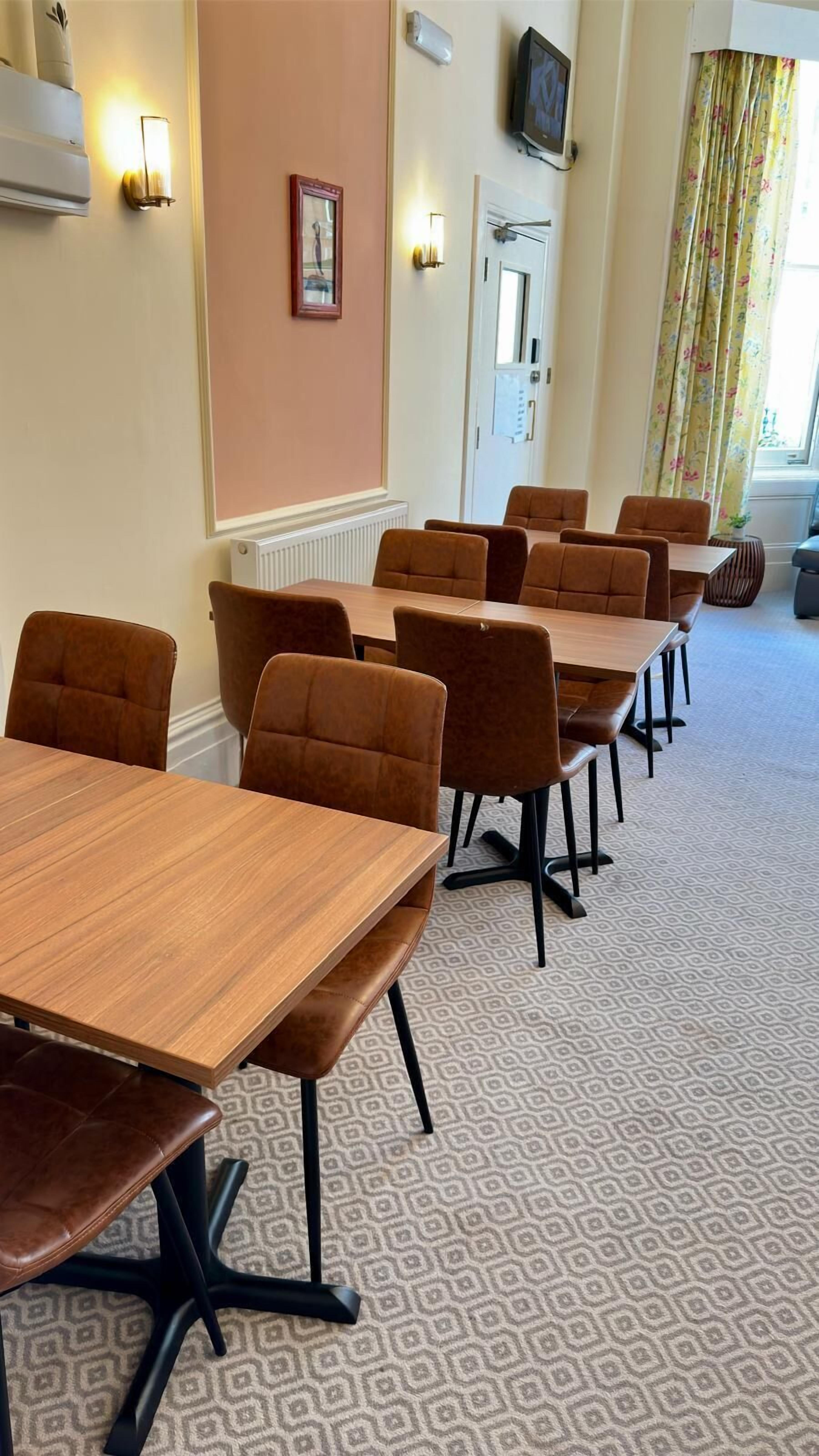 A conference room with multiple tables and chairs, a television on the wall, and a window with curtains.