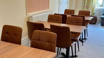 A conference room with multiple tables and chairs, a television on the wall, and a window with curtains.