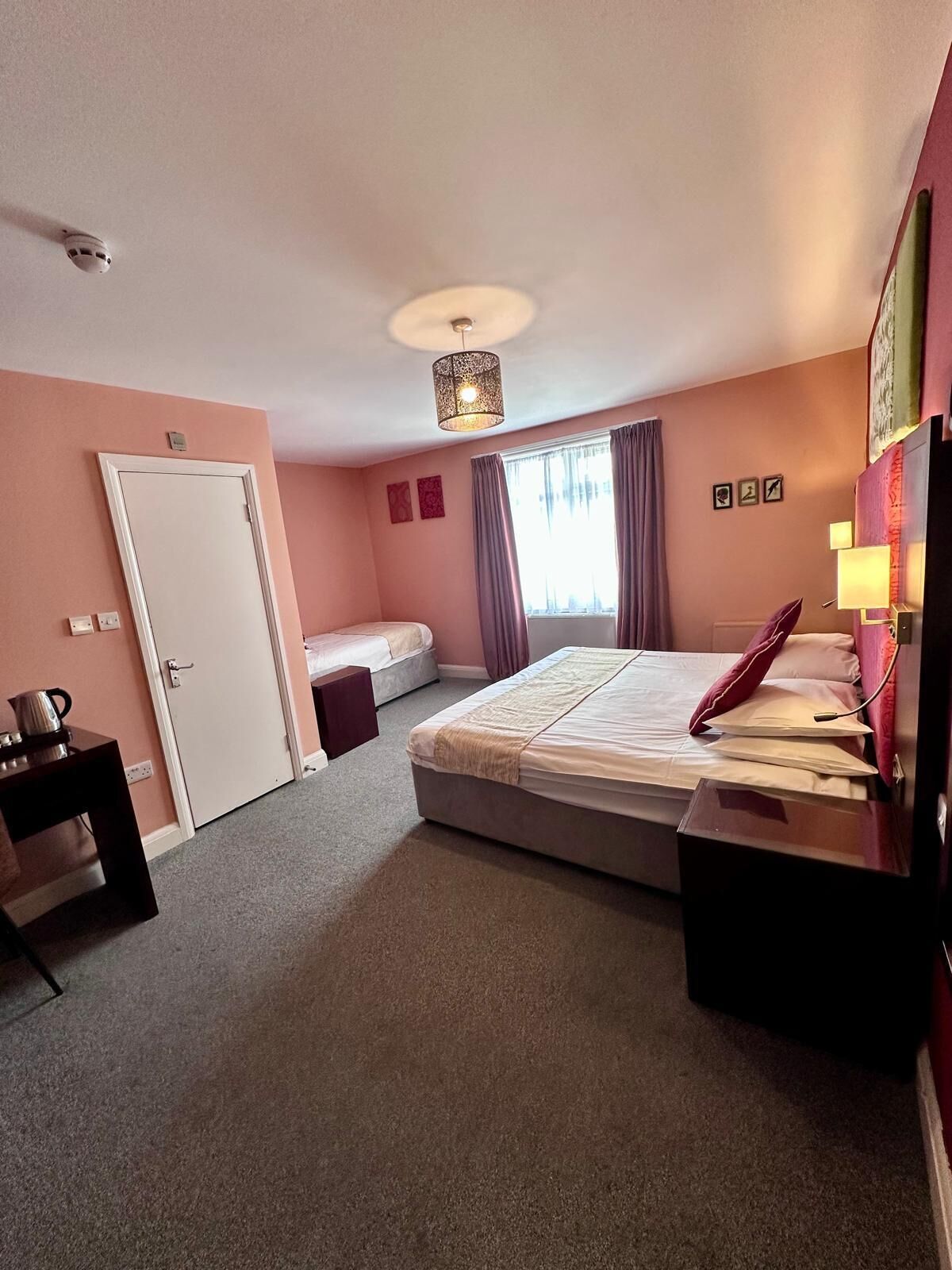 Een hotelkamer met een groot bed, een bureau, een stoel, een lamp en een raam met gordijnen.