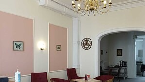 A hotel lobby with a chandelier, red upholstered chairs, a wooden side table, and a clock on the wall. - Acacia Hotel (London)